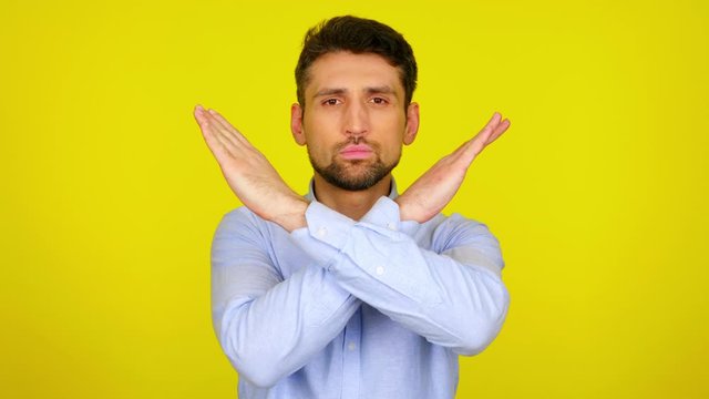 Stop concept: virus, violence, abortion, corruption, inequality, plastic, racism. Serious bearded man in a light blue shirt crossed his arms in front of his chest on yellow background with copy space