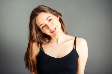 Fototapeta premium The girl with her hair in a black top smiles and is a happy man. Enjoy life. On a gray background. Without makeup, without retouching.