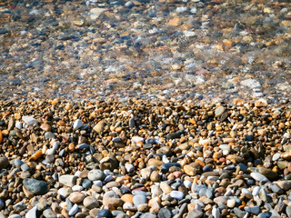Beautiful summer landscape. Background with small pebbles. Multi-colored sea pebbles covered with clear water. The shore of the beach with sand and pebbles washed by the waves of the sea. Color stones