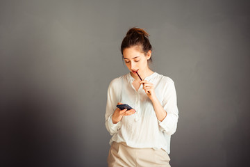 Serious girl with blindfolded hair on her head. With a phone in his hands. Portrait. On a gray...