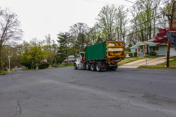 A green dumpster is being transported on the bed of a heavy duty truck on a street in a residential community