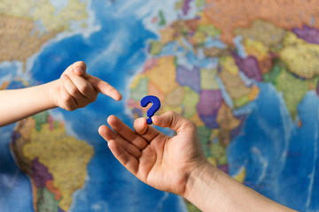 Adult and child hands holding question mark plastic toy on world political map background. Travel planning explore destination concept. Family holidays and time together. Quarantine over borders open