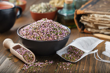Bowl of dry healthy heather, tea bag with Erica flowers inside. Tea cup, infusion bottle and books on background.