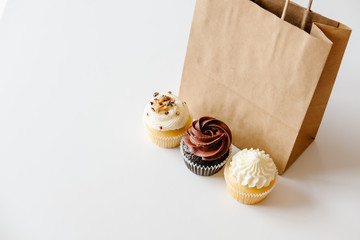 Vanilla, chocolate and caramel cupcakes and brown paper bag on white table background. Sweet food...