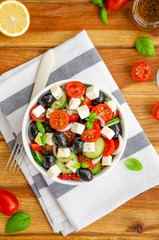 Greek salad of fresh juicy vegetables, feta cheese, herbs and olives in a white bowl on a wooden background. Healthy food. Vertical orientation. Top view.