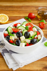 Greek salad of fresh juicy vegetables, feta cheese, herbs and olives in a white bowl on a wooden background. Healthy food. Vertical orientation.