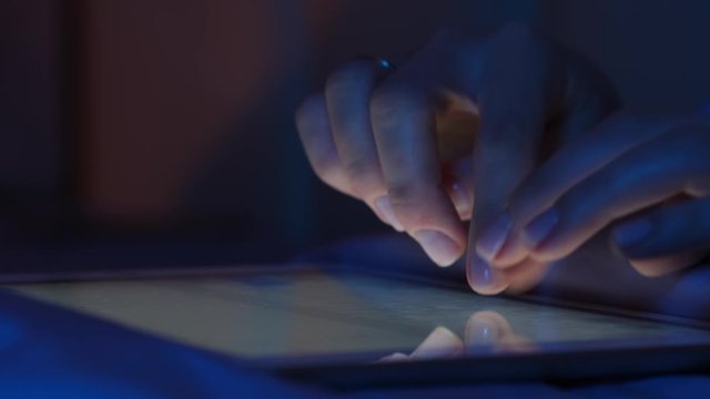 Close-up of tablet device with touch screen, girl is typing text message with her hands, scrolling screen with her finger in search of images and news on Internet.