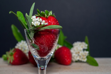 strawberry in a little decorated glass. strawbwrries and small white flowers in a composition in the background