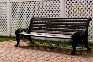 Empty dark wooden bench on the background of a white plastic fence in a rural village. Comfortable resting place under the open sky. Close-up, copy space.