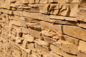 Blurred background of yellow slate stone surface. Blocks of artificial finishing stone for wall decoration. Rough stone background.