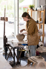 Fototapeta na wymiar Female potter making vase in workshop standing near window