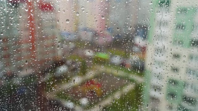 Raindrops on glass window. Water drops falling down on window pane in a rainy weather on city landscape.Wet drops on glass. Close-up.