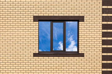 A three-pane window against a new brick wall. A fragment of a house wall for a construction-themed design. Clouds are reflected in the window.