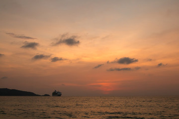 Fototapeta na wymiar A large trade ship arrives on the shores of Thailand against the backdrop of an orange sunset.
