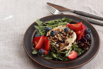 Baked goat cheese with honey, pine nuts, blueberries and strawberries on arugula pillow