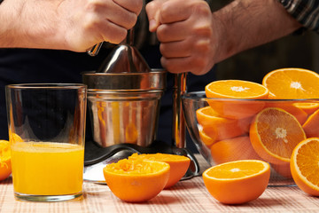 Squeezing an orange with a manual press, close view, making a glass of fresh. Fresh oranges on a wooden table, whole, squeezed and sliced.