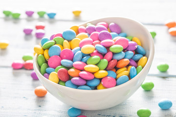Close up of a white bowl full of smarties with many placed randomly around