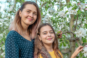 Family with flowers. Gorgeous mother and her daughter in the spring garden. The elegant girls near the tree in the spring