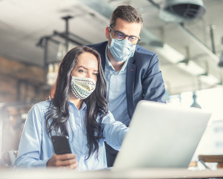 Good looking female and male coworkers look at the computer screen together, wearing face masks