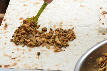 Girl sprinkles shawarma with a shovel with meat from a silver bowl.