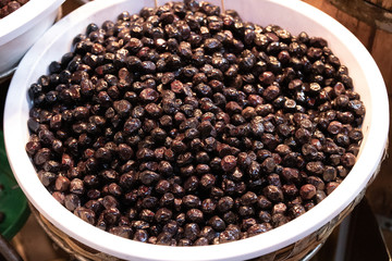 Black pickled olives are photographed on the counter in front of the market. Close up.
