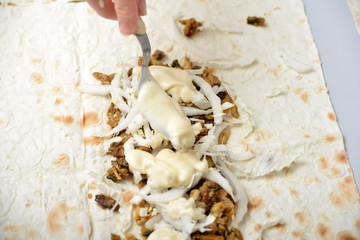 Girl sprinkles shawarma with mayonnaise on a fork.