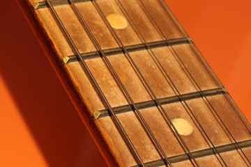 Acoustic guitar neck on an orange background. Part of a guitar on a bright background.