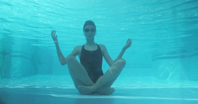 Young athletic woman sitting in lotus pose underwater in blue outdoor swimming pool