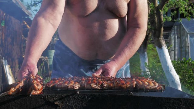 Fat funny man cooks kebabs and dances in the backyard. Unrecognizable man fries meat against the background of nature. The concept of gluttony and an idle lifestyle