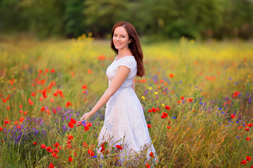 Naklejka na ściany i meble Portrait of a beautiful cute brunette girl in poppy field at sunset