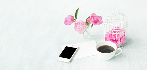 Small bird cage with peony flower bouquet, invitation card template with text space, smarphone device with black screen, small aroma coffee cup. Greeting card and white provence interior.