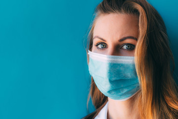 Close-up portrait of young female doctor in medical mask and white gown on blue background. Female doctor in clinic in surgical mask with space for text. Beautiful woman in hospital. Soft focused