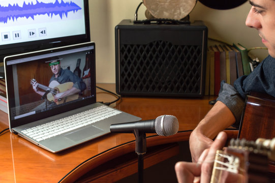 Young man recording himself while playing guitar and singing to share the video in social media. Musician recording a music video at home.