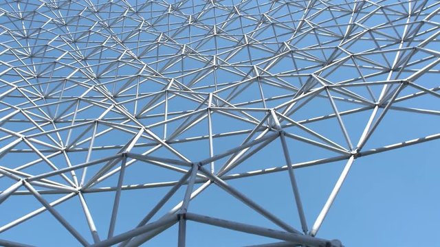 Low to high shot view of geodesic dome with a pan shot under a clear and cloudy, sky day surrounded with fresh trees outside museum