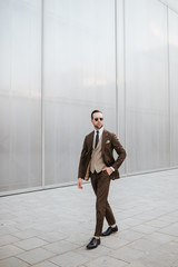 Fashion business wear model in brown suit and tie. Outdoor photoshoot in white wall background concept for magazine cover and man’s brochure clothing images.
