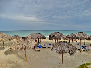 Fotografía de las tradicionales sombrillas con techo de ramas de palmera y hamaca color azul en la playa de Varadero, Cuba,  sin gente.