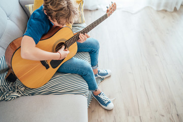 Preteen boy playing acoustic guitar dressed casual jeans, shirt and new sneakers sitting on the...