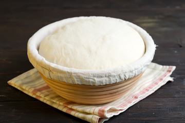 Freshly cooked yeast dough in a basket for baking of fresh natural cakes and cookies on a dark wooden background.