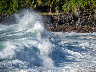 Big waves crash close to shore with aquamarine seas, white foam, sand and blue skies.