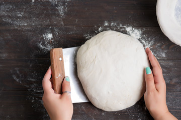 Woman's hand hold fresh dough and cutter scraper for preparing homemade bread on a wooden dark background.