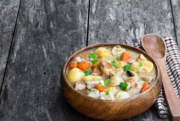 Stewed pork with vegetables in wooden bowl on rustic table