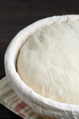 Freshly cooked yeast dough in a basket for baking of fresh natural cakes and cookies on a dark wooden background.