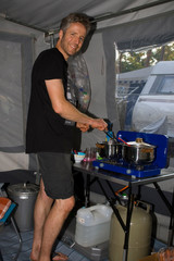 Mann kocht im Campingurlaub in einem Zelt an einem Gaskocher