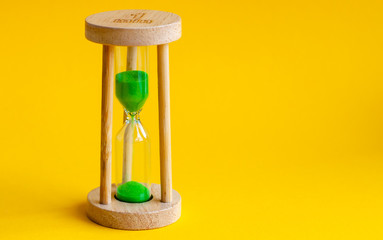 Hourglass with green sand inside on a yellow background
