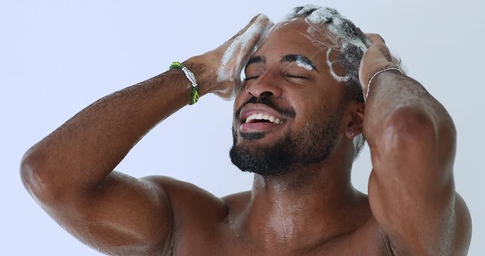 Smiling young adult handsome african man washing head with anti-dandruff shampoo taking shower. Happy hipster afro american guy enjoying everyday fresh clean hair care routine. Male haircare concept.