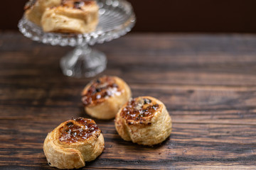 Homemade glazed puff pastry cinnamon rolls with custard and raisins on wooden background.