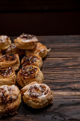 Homemade glazed puff pastry cinnamon rolls with custard and raisins on wooden background.