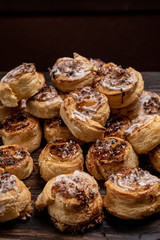 Homemade glazed puff pastry cinnamon rolls with custard and raisins on wooden background.