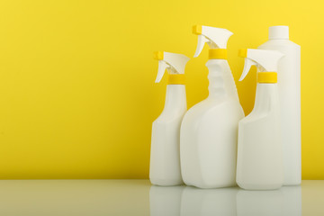 cleaning products in white spray bottles on yellow background with copy space 