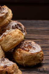 Homemade glazed puff pastry cinnamon rolls with custard and raisins on wooden background.